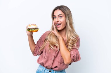 Genç, güzel Uruguaylı bir kadın elinde hamburgerle beyaz arka planda izole edilmiş bir şekilde bir şeyler fısıldıyor.
