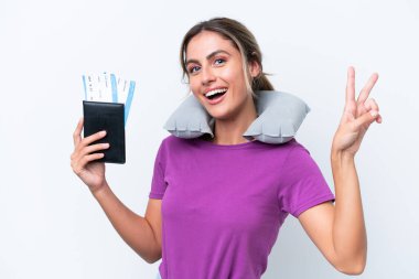 Şişirilebilir Seyahat Yastığı ile genç ve güzel Uruguaylı kadın beyaz arka planda izole edilmiş gülümseyerek zafer işareti gösteriyor.