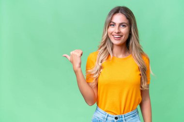 Genç Uruguaylı kadın, izole edilmiş arka planda bir ürünü sunmak için kenarı işaret ediyor.