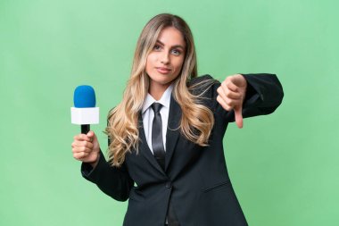 Genç, güzel Uruguaylı televizyon sunucusu, izole edilmiş arka planda, olumsuz ifadeyle baş parmağını aşağı gösteriyor.