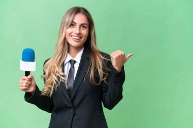 Genç ve güzel Uruguaylı televizyon sunucusu izole edilmiş bir arkaplanda bir ürünü sunmak için kenarı işaret ediyor.