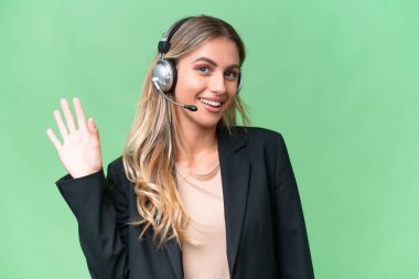 Tele pazarlamacı güzel Uruguaylı kadın izole bir arka planda kulaklıkla çalışıyor mutlu bir ifadeyle selam veriyor.