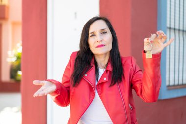 Orta yaşlı bir kadın evin anahtarlarını açık havada tutuyor. Omuzlarını kaldırırken şüpheli hareketler yapıyor.