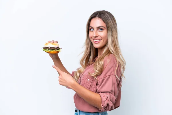 Młoda Ładna Urugwajska Kobieta Trzyma Hamburgera Białym Tle Wskazuje — Zdjęcie stockowe