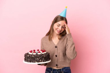 Litvanyalı genç bir kadın pembe arka planda izole edilmiş doğum günü pastası tutuyor ve gülüyor.
