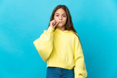 Küçük kız izole edilmiş mavi arka planda sessizlik işareti gösteriyor.