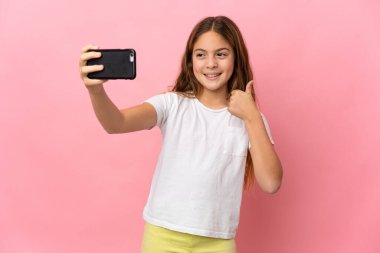 İzole edilmiş pembe arka planı olan çocuk cep telefonuyla selfie çekiyor.