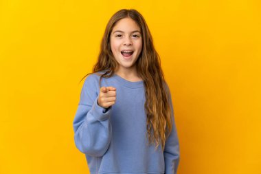 İzole edilmiş sarı arka plandaki çocuk şaşırmış ve ön tarafı işaret ediyor