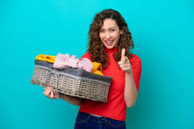 Mavi arka planda bir çamaşır sepetini tutan beyaz bir kadın. Başparmakları havada. Çünkü iyi bir şey oldu.