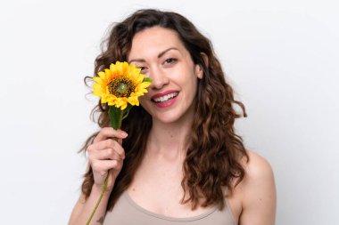 Beyaz arka planda izole edilmiş beyaz tenli genç bir kadın gülümserken elinde bir ayçiçeği tutuyor. Portreyi kapat
