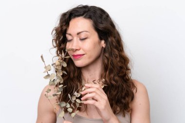 Beyaz arka planda, elinde okaliptüs dalı tutan beyaz tenli bir kadın. Portreyi kapat