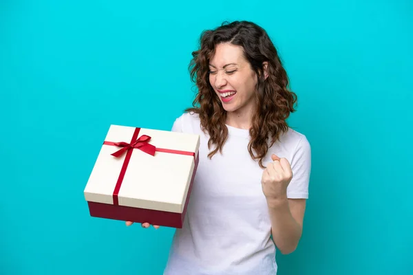 stock image Young caucasian woman holding a gift isolated on blue background celebrating a victory