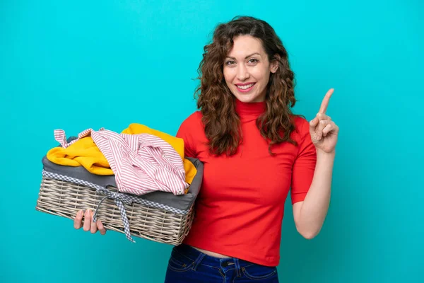 stock image Young caucasian woman holding a clothes basket isolated on blue background pointing up a great idea