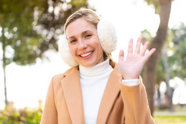 Sarışın genç bir kadın, açık havada kışlık kuklalar takıyor ve mutlu bir ifadeyle selamlıyor.