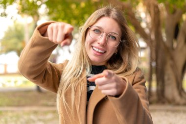 Açık havada güzel sarışın bir kadın gülümserken seni işaret ediyor.