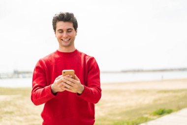 Genç yakışıklı adam cep telefonuyla mesaj yolluyor.
