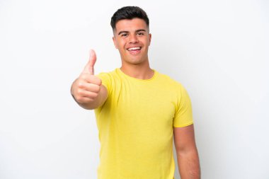 Beyaz arka planda izole edilmiş beyaz tenli yakışıklı bir genç. Başparmakları havada. Çünkü iyi bir şey oldu.