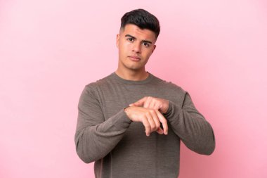 Pembe arka planda izole edilmiş beyaz, yakışıklı bir adam geç kalma jesti yapıyor.