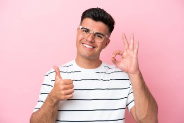 Pembe arka planda gözlüklü, beyaz tenli yakışıklı bir adam var.