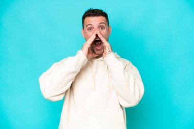 Beyaz tenli yakışıklı adam mavi arka planda izole edilmiş bağırıyor ve bir şeyler söylüyor.