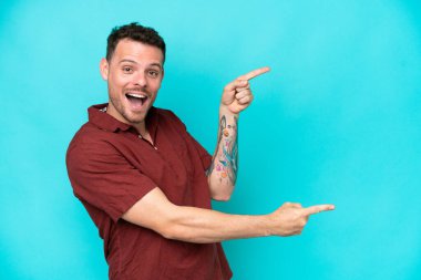 Mavi arka planda izole edilmiş beyaz tenli yakışıklı bir adam, parmağını yana uzattı ve bir ürün sundu.
