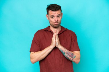 Mavi arka planda izole edilmiş beyaz tenli yakışıklı adam avuç içlerini bir arada tutuyor. İnsan bir şey ister.