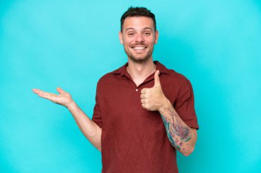 Beyaz tenli yakışıklı adam mavi arka planda izole edilmiş. Kopyalama alanı hayali bir şekilde avucunun içinde duruyor. Bir ilan vermek için.