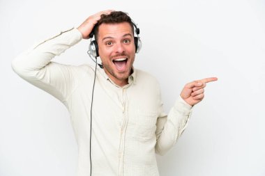 Tele pazarlamacı beyaz arka planda izole edilmiş kulaklıkla çalışan beyaz bir adam şaşırmış ve parmağıyla kenarı işaret ediyor.