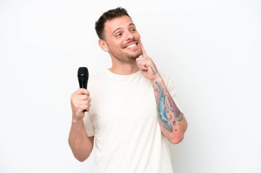 Young caucasian singer man picking up a microphone isolated on white background thinking an idea while looking up