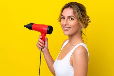 Young Uruguayan woman holding a hairdryer isolate don yellow background smiling a lot