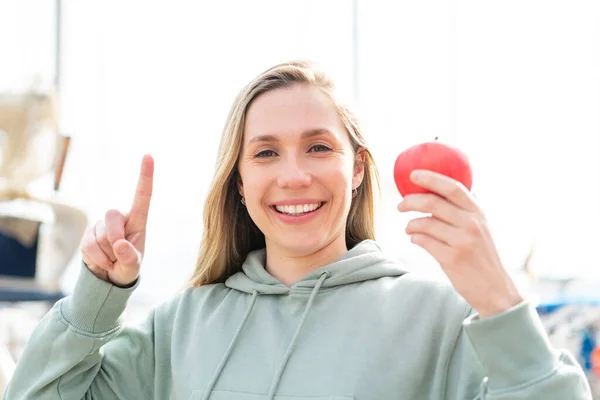 一个年轻的金发女人在户外拿着一个苹果 提出了一个伟大的想法 — 图库照片