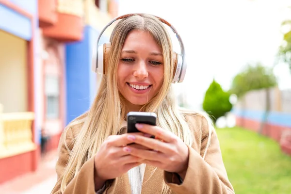 Молодая Симпатичная Блондинка Улице Слушает Музыку Смотрит Мобильный Телефон — стоковое фото