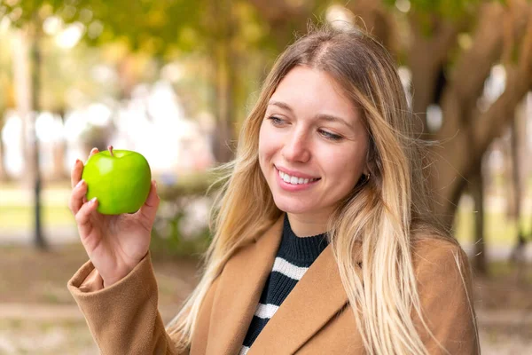年轻漂亮的金发女人 在户外拿着一个苹果 满面春风 — 图库照片