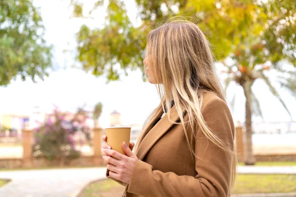 年轻漂亮的金发女人背着咖啡站在室外 — 图库照片
