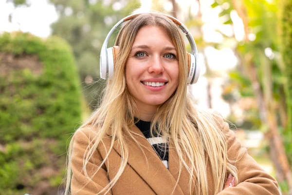 Νεαρή Όμορφη Ξανθιά Γυναίκα Ακούει Μουσική Ακουστικά Εξωτερικούς Χώρους Κρατώντας — Φωτογραφία Αρχείου