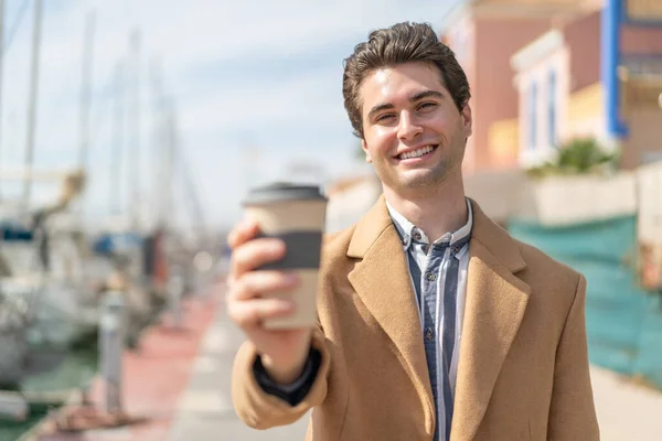 年轻英俊的男人拿着一杯带着快乐表情的咖啡走了 — 图库照片