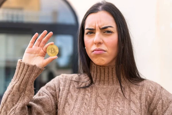 Dışarıda Bitcoin tutan genç bir kadın üzgün bir ifadeyle