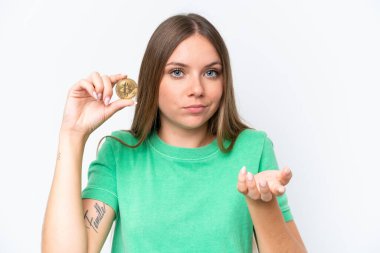 Beyaz arka planda izole edilmiş Bitcoin tutan güzel sarışın kadın omuzlarını kaldırırken şüpheyle hareket ediyor.