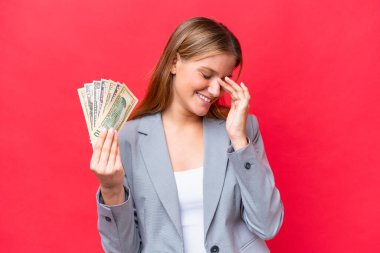 Young business caucasian woman holding money isolated on red background laughing