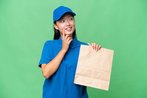 年轻的亚洲女人提着一袋外卖食品而不顾孤立的背景 一边抬头看一边想办法 — 图库照片
