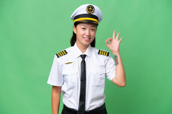飞机驾驶员亚洲女人越过孤立的背景 用手指显示好的标志 — 图库照片