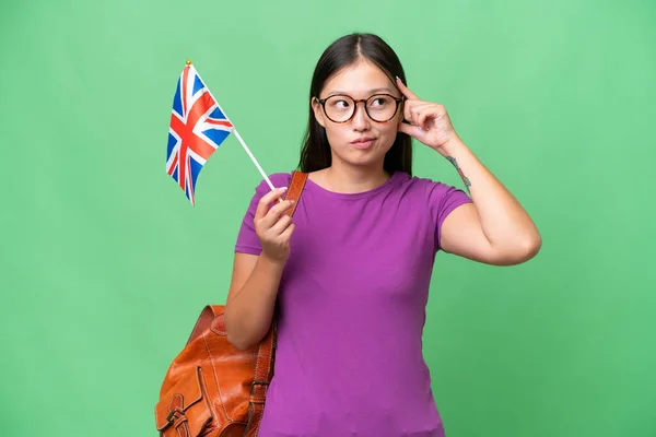 Młoda Azjatka Trzymająca Flagę Zjednoczonego Królestwa Odosobnionym Tle Mająca Wątpliwości — Zdjęcie stockowe