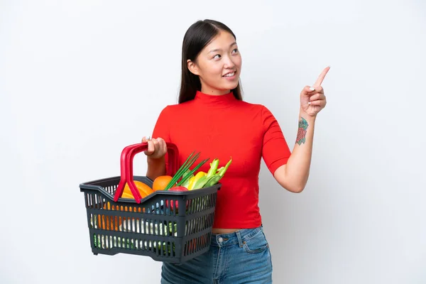白い背景に隔離された食べ物でいっぱいのショッピングバスケットを持っている若いアジアの女性は素晴らしいアイデアを指摘 — ストック写真