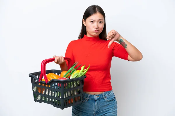 年轻的亚洲女人拿着一篮子被白色背景隔离的食物 带着负面的表情垂头丧气 — 图库照片