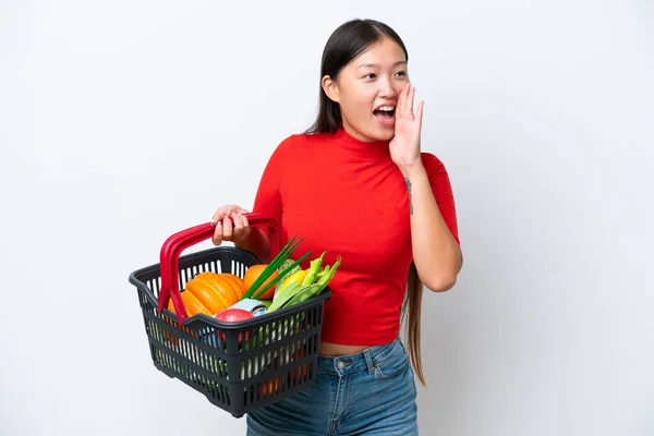 年轻的亚洲女人拿着一个购物篮 里面塞满了被白色背景隔离的食物 大喊着 旁边张着大嘴 — 图库照片