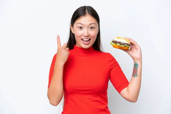 Młoda Azjatka Trzyma Hamburgera Białym Tle Wskazując Świetny Pomysł — Zdjęcie stockowe