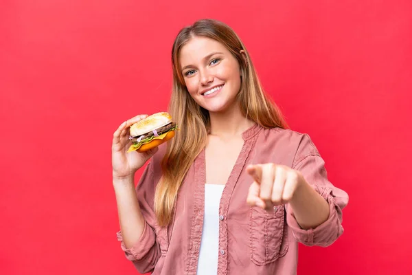 年轻的高加索女人拿着一个用红底指尖指着你的汉堡包 带着自信的表情 — 图库照片
