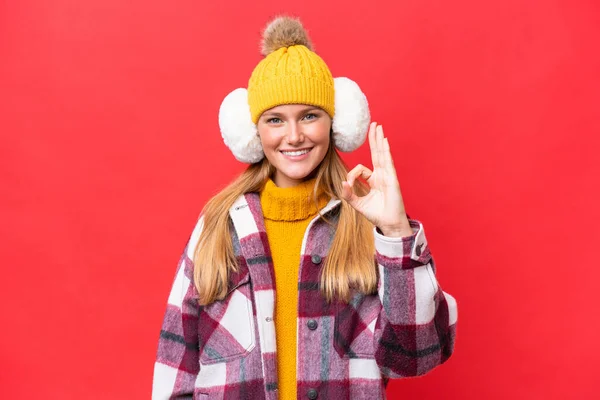 Νεαρή Όμορφη Γυναίκα Φορώντας Muffs Χειμώνα Απομονώνονται Κόκκινο Φόντο Δείχνει — Φωτογραφία Αρχείου
