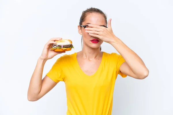 Młoda Biała Kobieta Trzymająca Hamburgera Białym Tle Zakrywająca Oczy Dłońmi — Zdjęcie stockowe