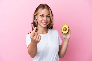 Avokado tutan genç Rus kadın pembe arka planda izole edilmiş.